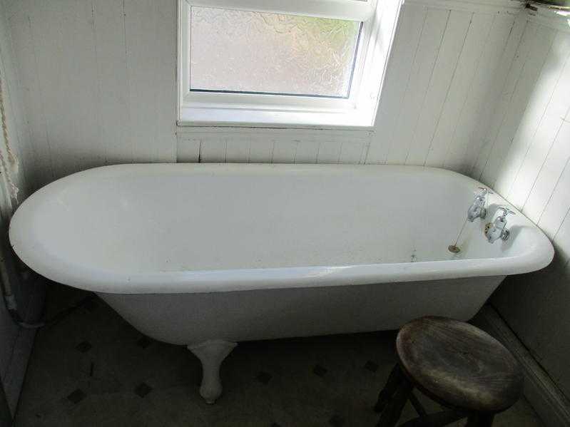 Old cast iron roll-top bath on legs, and washbasin for pedestal